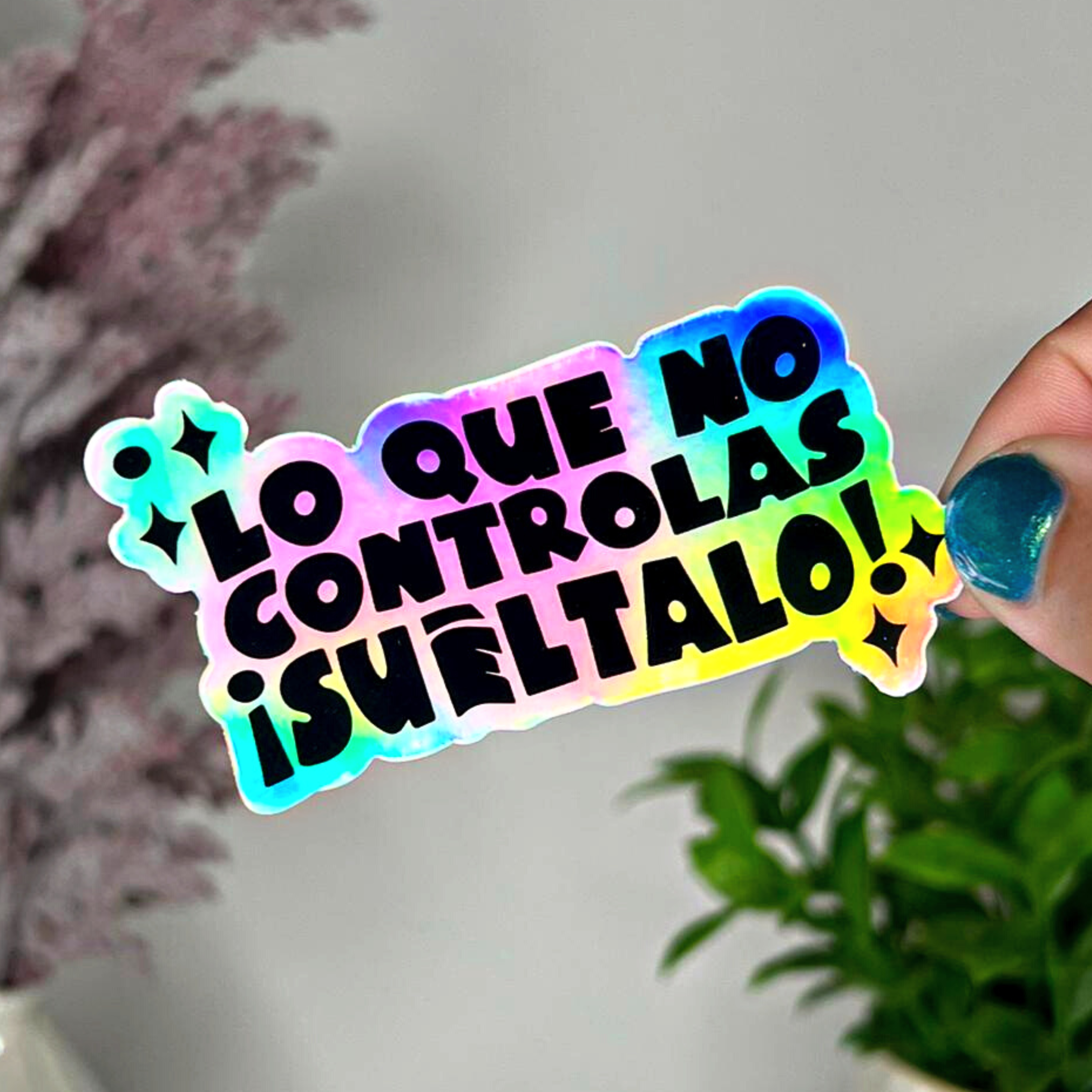 Sticker holográfico con frase motivacional “Lo que no controlas, suéltalo”, sostenido con mano sobre fondo decorativo – ideal para planners, journaling y decoración emocional.